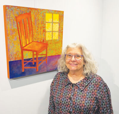  Artist Lori Zurvalec stands next to “Absent in Physical Presence Only,” a  painting of her late father’s chair that’s on display in her new solo show. 