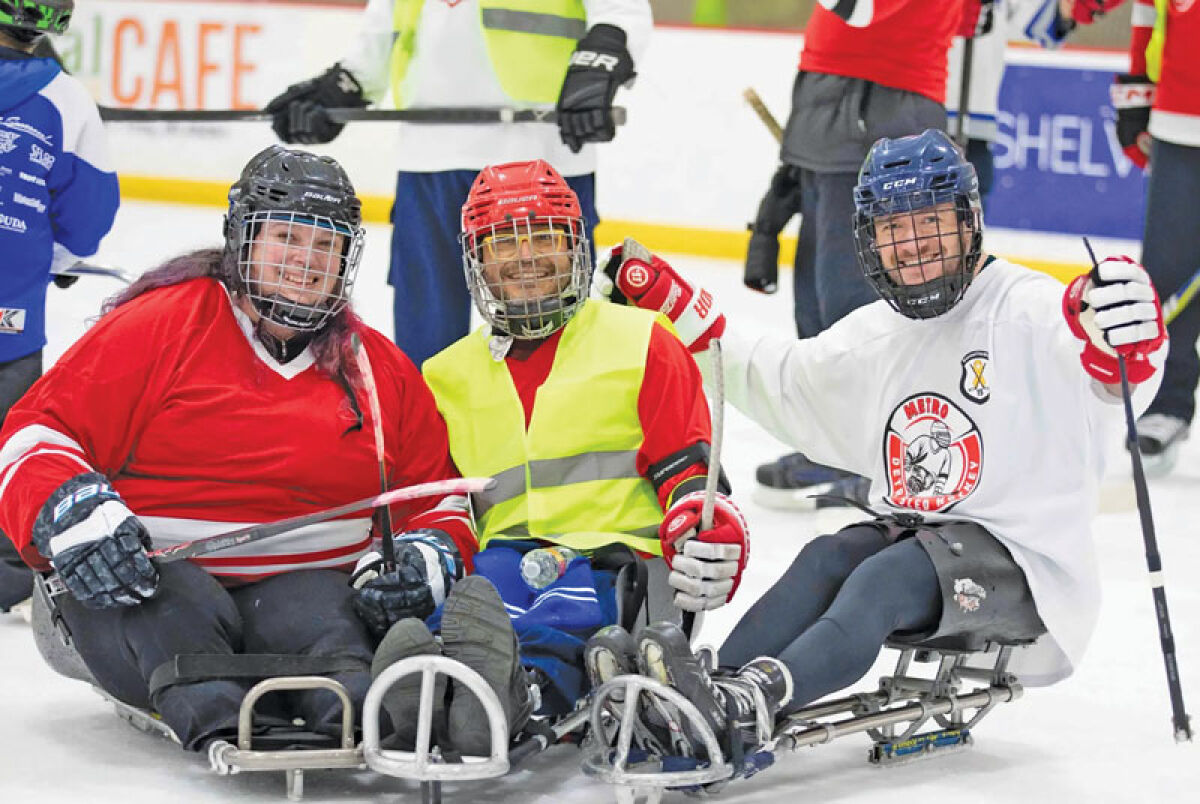  Three participants pose on their sleds during a sled hockey game from a previous Hockey Mentors event. 
