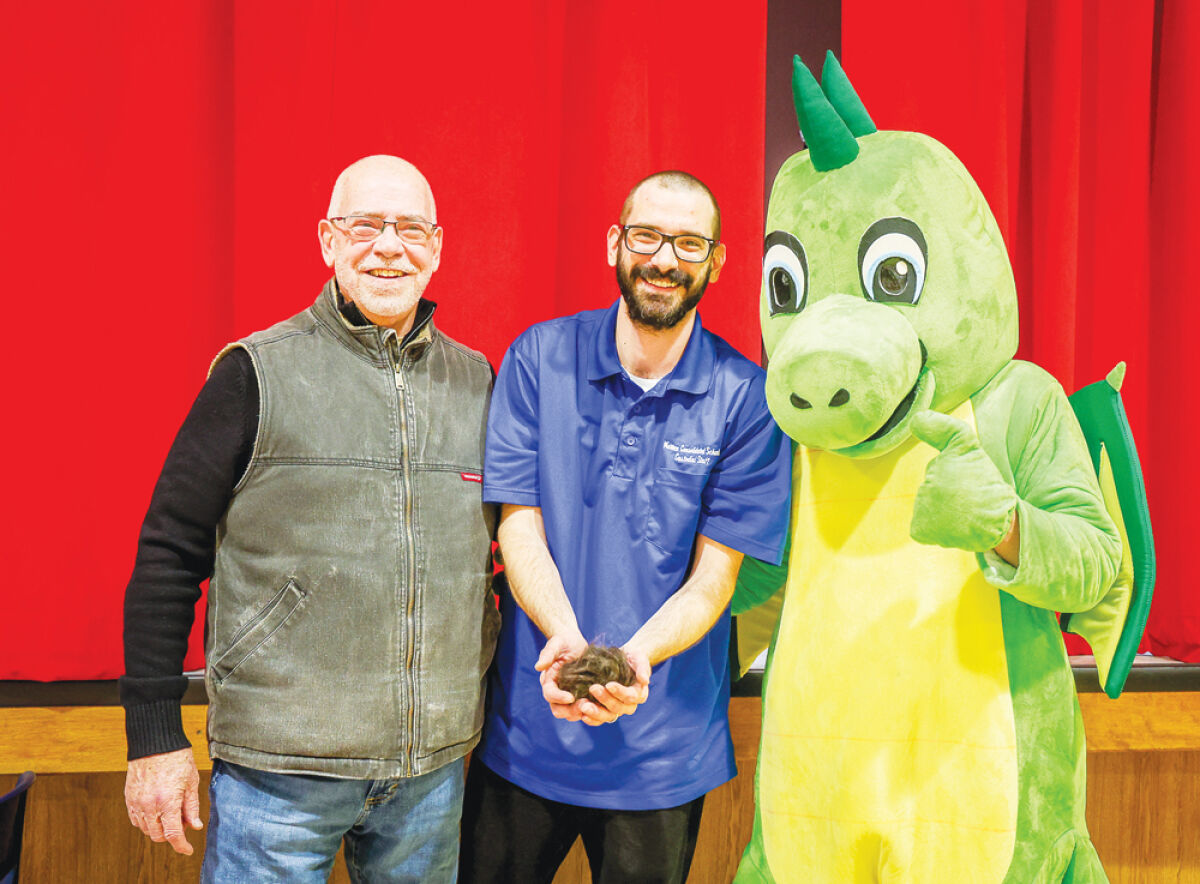  Susick Elementary School head custodian Adam Wilson, center, volunteered to have his head shaved March 12 as an incentive to motivate students to read during March is Reading Month. His dad, David Wilson, left, is a retired Warren Consolidated Schools educator who also shaved his head during his teaching days to encourage students to read. On the right is the school mascot, Drako. 