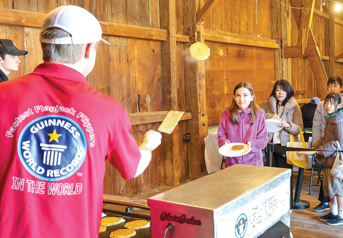 Hayden Hubel, of Chris Cakes, flips a pancake to Eleanor Kruk, 11, of Farmington Hills, during MapleFest at Tollgate Farm. 