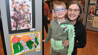  Five-year-old Dashiell Neumann is joined by his mom, Ashly, at the student art show April 18. Dashiell&rsquo;s painting is at the bottom with the orange trim.  