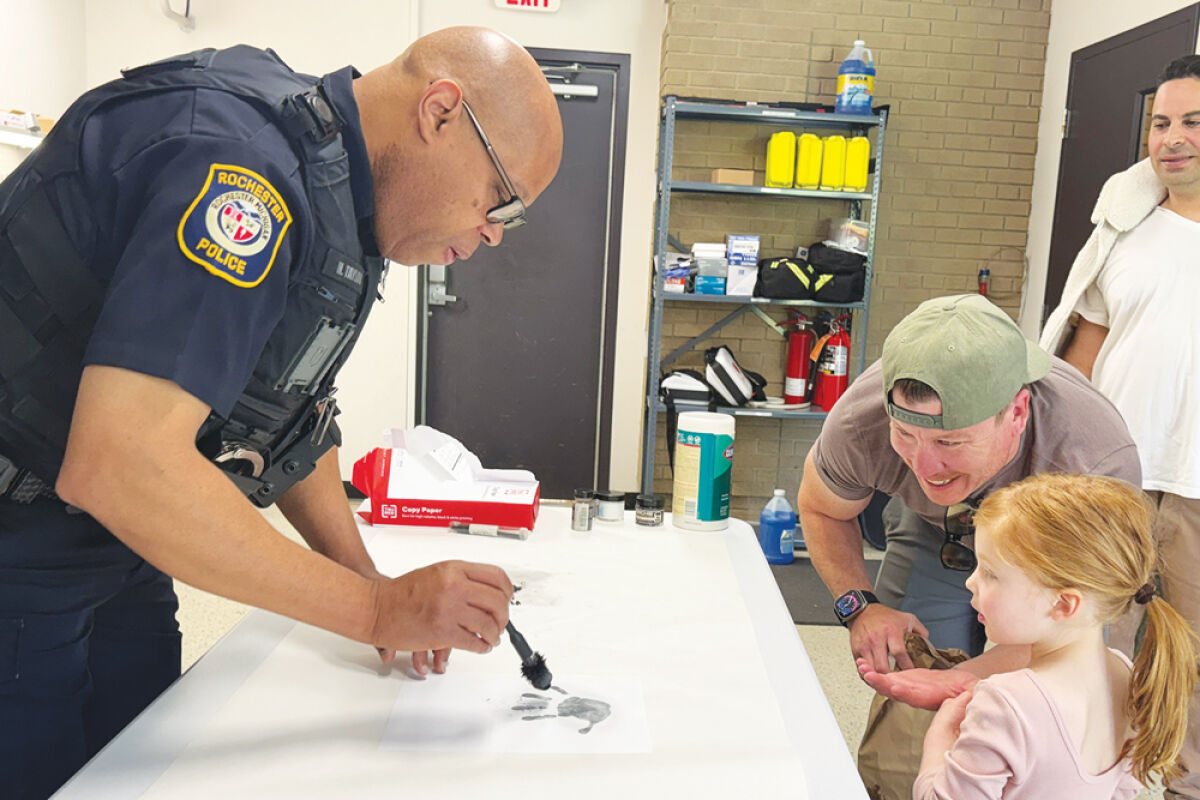  Rochester police officer and evidence technician Merlin Taylor shows Vivienne Kardes, 3, with her dad, Michael Kardes, of Oakland Township, how to dust her handprint during last year’s police open house. 