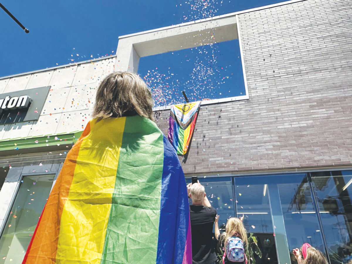  A child wearing a rainbow flag cape looks up at confetti flying in the sky. 