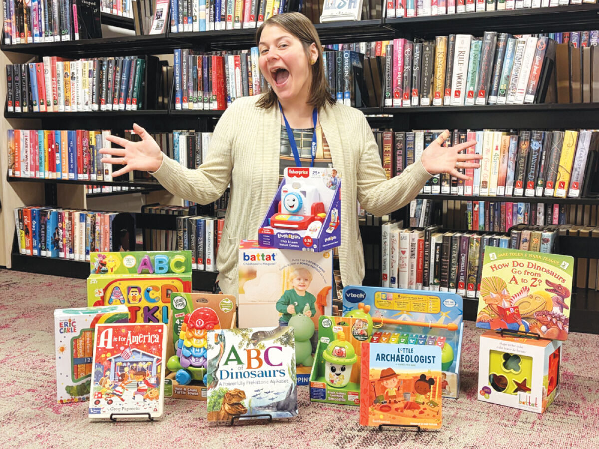  Sterling Heights Library Public Relations and Programs Coordinator Anneliese White shows some of the 2026 summer reading baby weekly raffle prizes. The grand raffle prize is a Little Tikes Cozy Coupe Dinosaur Car. 