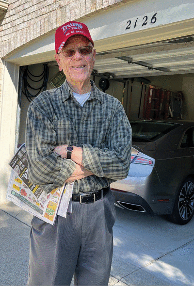  A recent photo of Clarence Arens in the driveway holding a newspaper containing one of his favorite hobbies, the crossword puzzle.   
