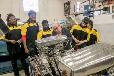  On Feb. 2, during filming, Paul Tregembo Sr. works with students to change the carburetor on a car that will be at Autorama. 