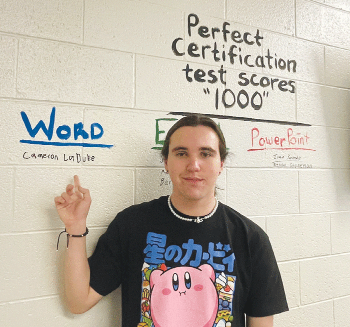  Cameron LaDuke points to his name, which is inscribed on the wall of teacher Tina Steele’s classroom with the names of other students who have achieved perfect scores on various Microsoft Office certification exams. 
