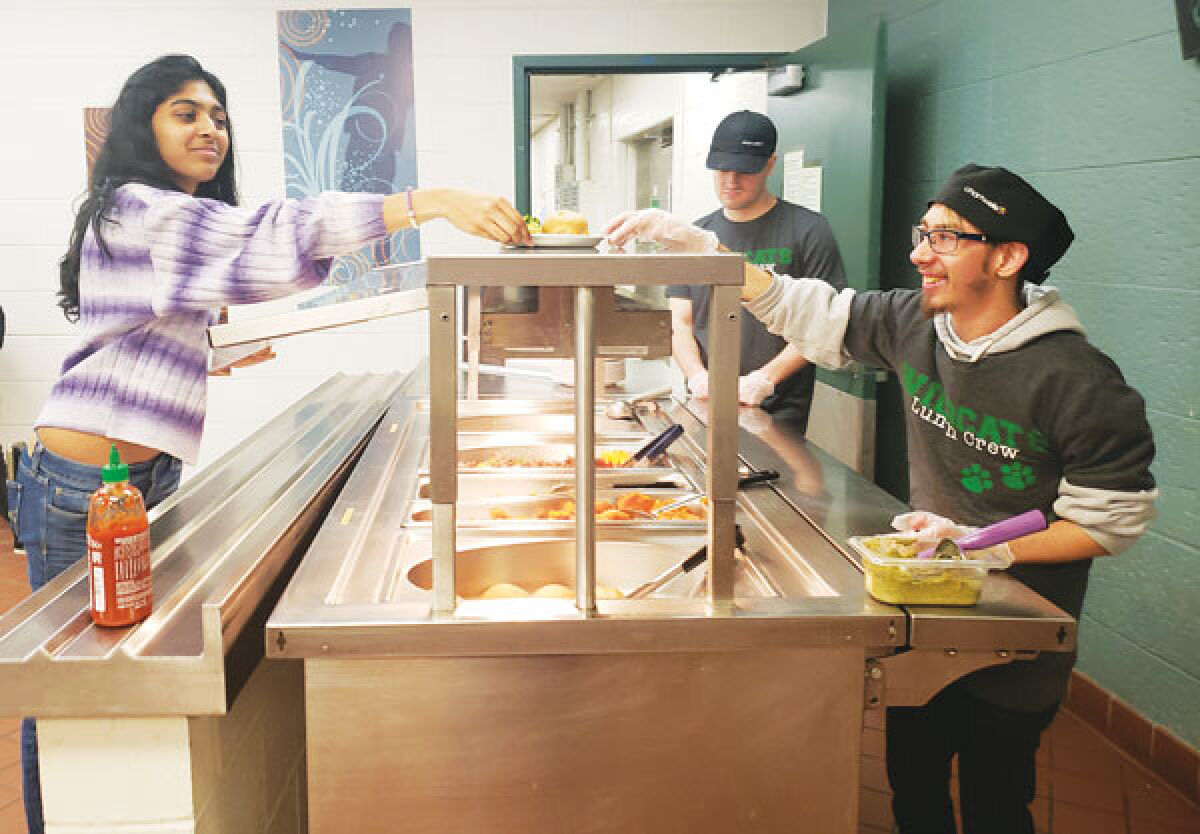  Hunter Goodman serves food at the Novi High School cafeteria to sophomore Meghna Routhu. In the background is Matt Heslop. Goodman and Heslop were students at the Novi Adult Transition Center and found their new jobs with the district through the center. 