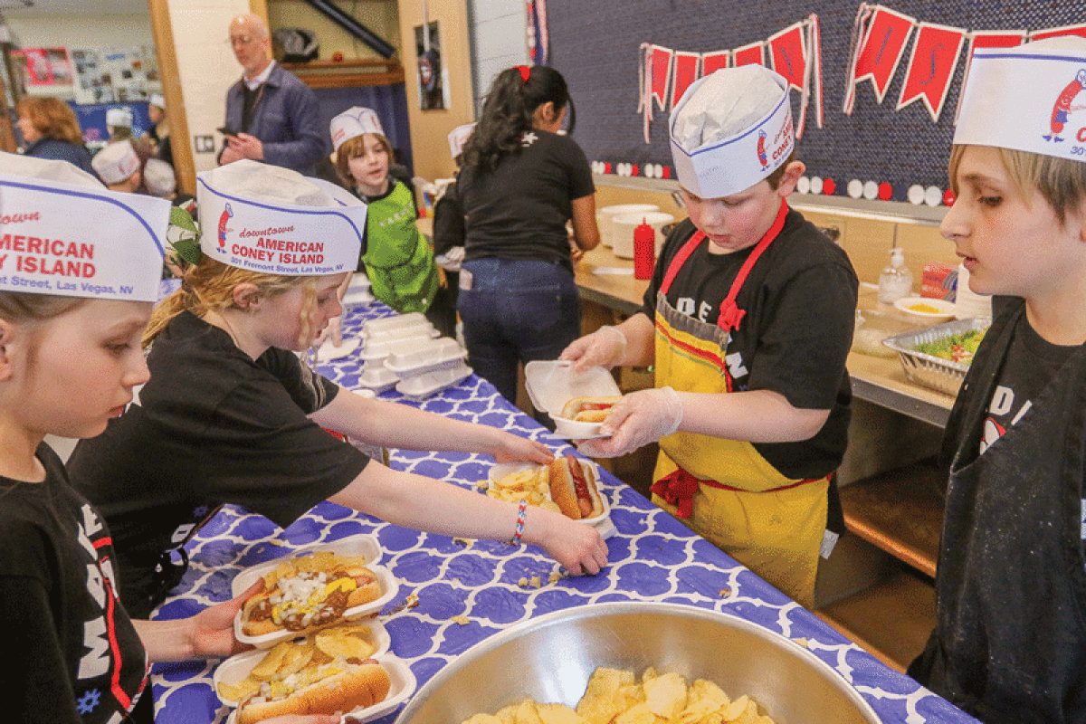  Student waitstaff collect orders from the cooks to deliver to diners seated in the classroom for the American Coney Island restaurant event at Ferry Elementary School March 16.  