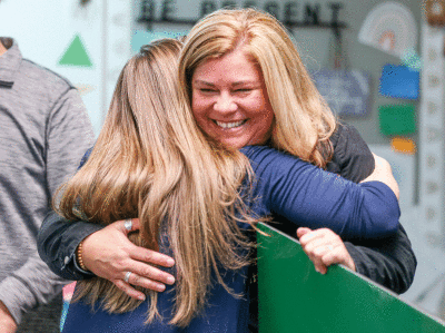  Sarah Laurence, a second grade teacher at Simonds Elementary in the Lamphere Schools and Oakland County’s Elementary School Teacher of the Year, gets a hug from the school’s principal, Rachael Wenskay, after learning of  her award March 22.  