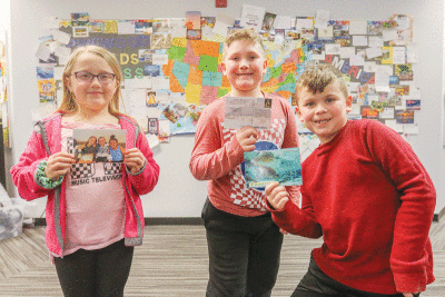  From left, Pinewood Elementary School third grader Abbygail Chapoton, third grader Joey Hill and second grader Maxwell Hill were among the students who received the most postcards addressed to them. Chapoton’s is holding up her favorite postcard of three cousins she has never met from Massapequa, New York. 