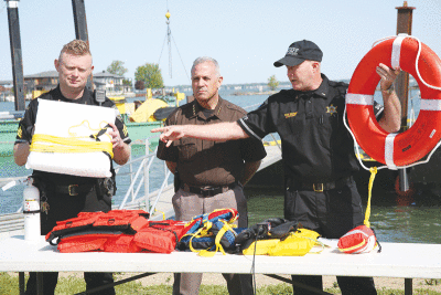  Pictured left to right, Sgt. Jamie Bagos, Sheriff Anthony Wickersham and Lt. Gary Wiegand, of the Macomb County Sheriff’s Office, showed off a variety of safety equipment at a boating safety press conference on May 25. Bagos and Wiegand hold two versions of a Type IV throwable device. 