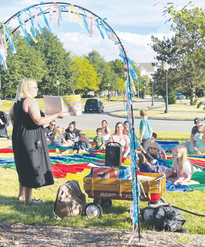  Wendy Lehman, the director of the library’s youth services department, reads a book to youth outside. 