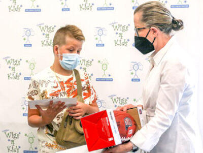  Maggie Varney, founder and CEO of Maggie’s Wigs 4 Kids of Michigan, right, presents Irvin with an NFL football signed by athlete Chris Maragos. 