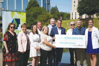  Gerard Santoro, program director for the Macomb County Planning and Economic Development (MCPED) department’s Land and Water Resources Group, left, and Christopher Fultz, Consumers Energy vice president of natural gas operations, unveil a $250,000 check for the Green Macomb Urban Forest Partnership. 