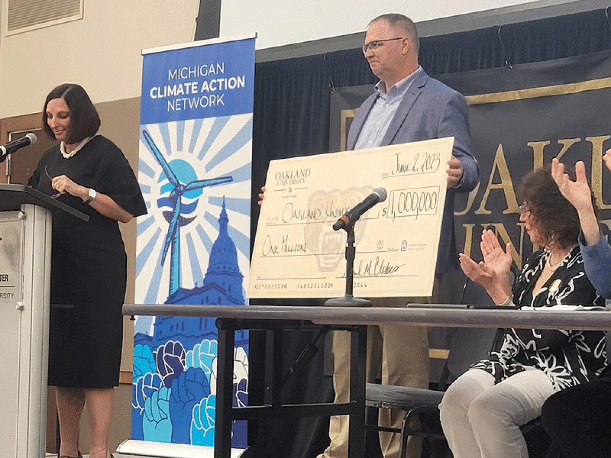  The OUCU gift was announced by April M. Clobes, left, OUCU president and chief executive  officer, and the check was presented by Steven J. Kurncz, OUCU board secretary, at the June 2 Michigan Climate Summit held at Oakland University. Oakland University President Ora Hirsch Pescovitz, right, applauds. 