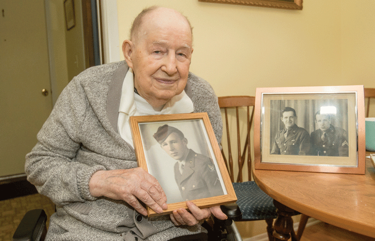  Alfred Bury, of Warren, holds up a photo of himself when he was in the service during World War II. On the table next to him is a photo of his brother Leonard, left, and Bury on the right. They both served their country during the war. 