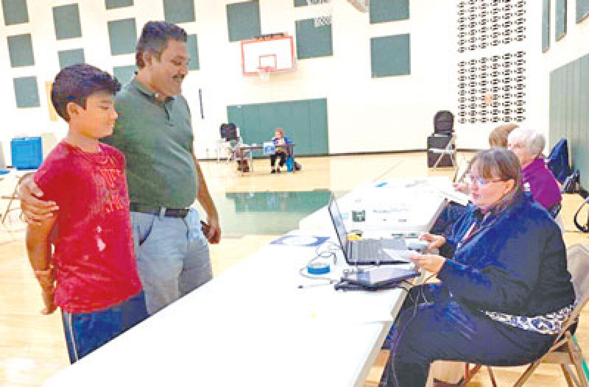  Ravi Ramamurthy wraps his arm around his 11-year-old son, Shiv, while showing him the process and importance of voting during the Aug. 8 election at the Novi Middle School polling location. Also pictured are election inspectors Michelle LaLonde and Mary Devlin. 