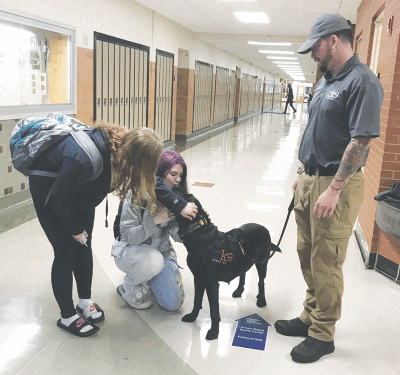   Lincoln High School seniors Ashley Blackwell, left, and Faith Shoults, center, get to know Binx while handler John Guerrero stands by.   