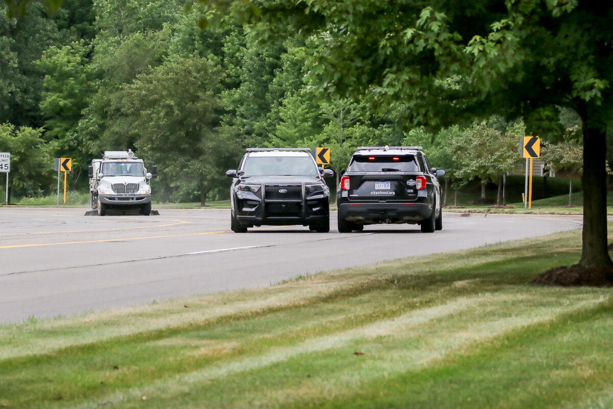  Police confer and a street sweeper works at the site of a fatal crash along Novi Road, south of 13 Mile Road, just prior to reopening the road during the early afternoon July 13. 
