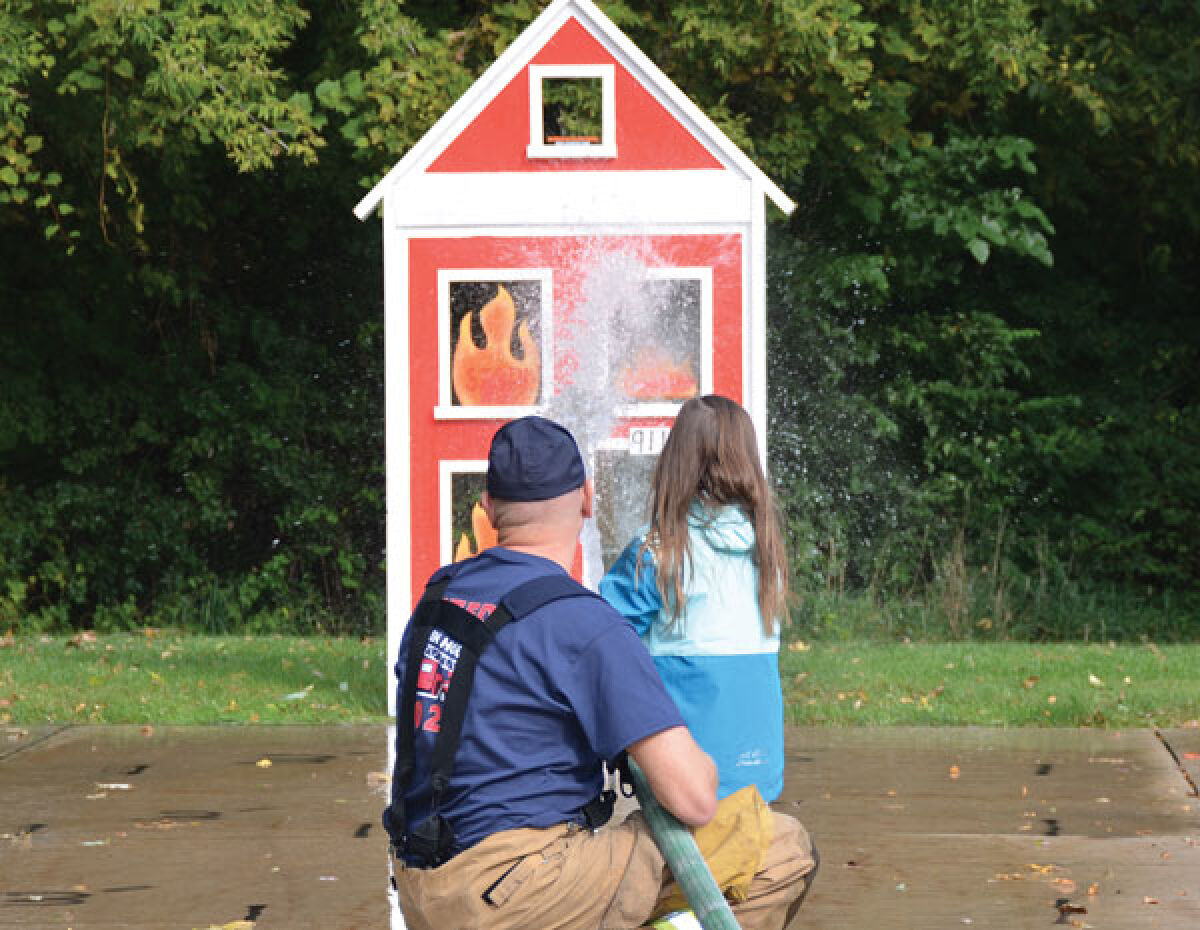  A firefighter helps a guest “put out” a house fire at the Macomb Township Fire Department’s open house on Oct. 8. 
