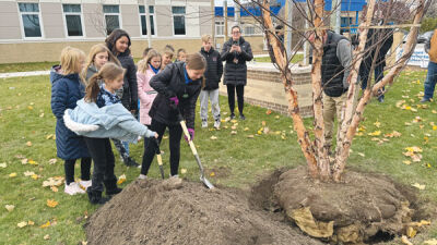  Ardmore Elementary School students take turns shoveling dirt onto a tree planted in the ground. 