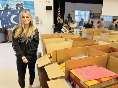  Eighth grader Paityn Gallo, the National Junior Honor Society president at Richards Middle School in Fraser, stands beside some of the food parcels collected in the school district. 