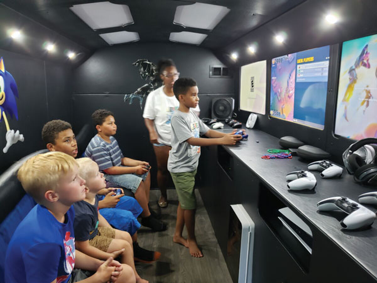  Jaylen Staley, 11, co-owner of Level Up Wit Jay, plays video games on his company bus with some of his friends July 22. His mom, Brittani Staley, pictured in back, said that neighborhood children will often come by just to see if the bus is open to play video games with Jaylen. 