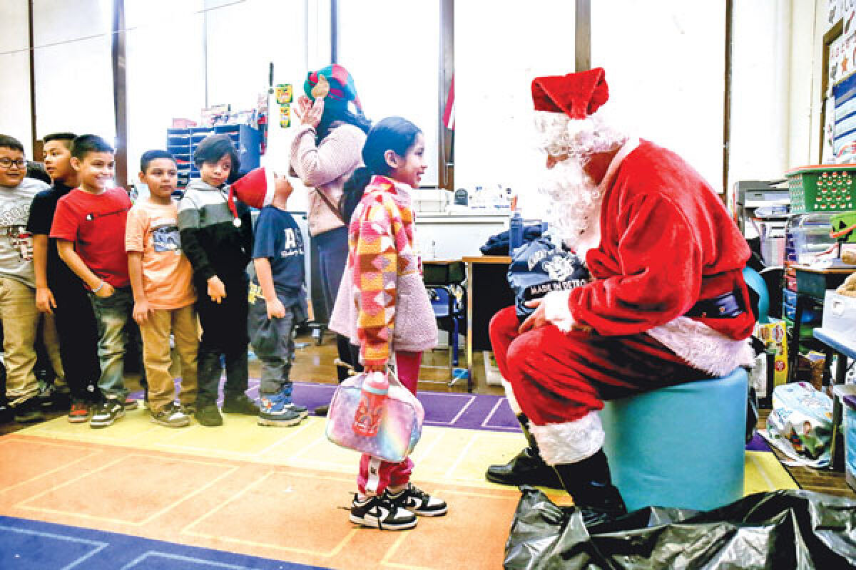  Novi Meadows sixth grade teacher Chip McDonald portrays Santa as he hands out gifts to a second grade student at the Academy of the Americas in Detroit on Dec. 14. 