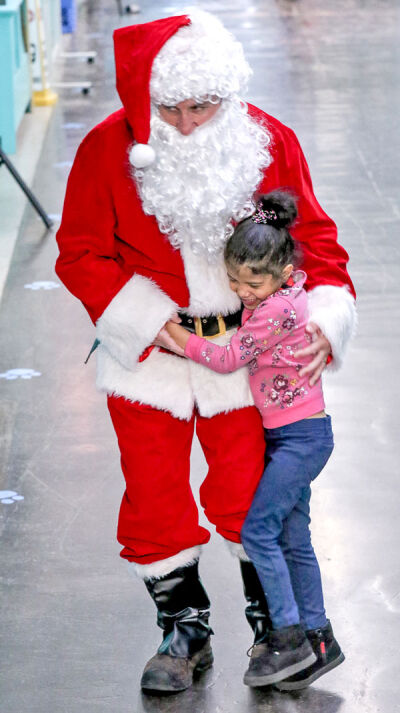  A young girl from the Academy of the Americas hugs former Novi Woods Elementary School Principal David Ascher as he portrays Santa Claus. 