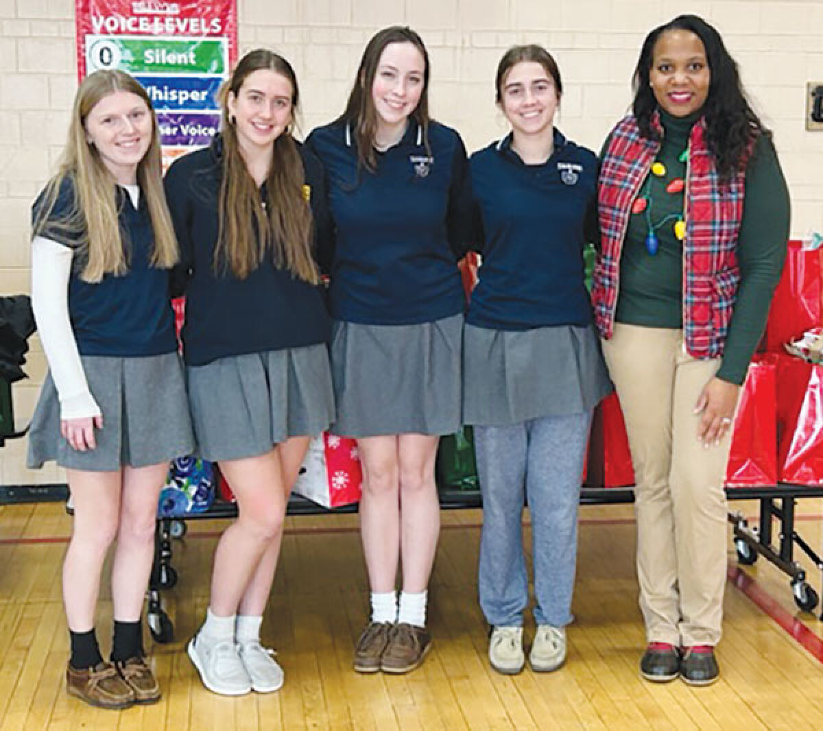  NHS officers Grace Plunkey, Catherine Murray, Madeleine Davidson and Thea Dugan stand with Brewer Academy social worker Marcia Gregory in front of a table full of gifts. 