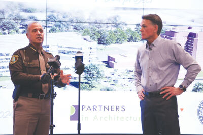  Macomb County Sheriff Anthony Wickersham, left, and Macomb County Executive Mark Hackel discuss the central intake and assessment center project on Jan. 18. A concept design for the new building is on the screen behind them. 