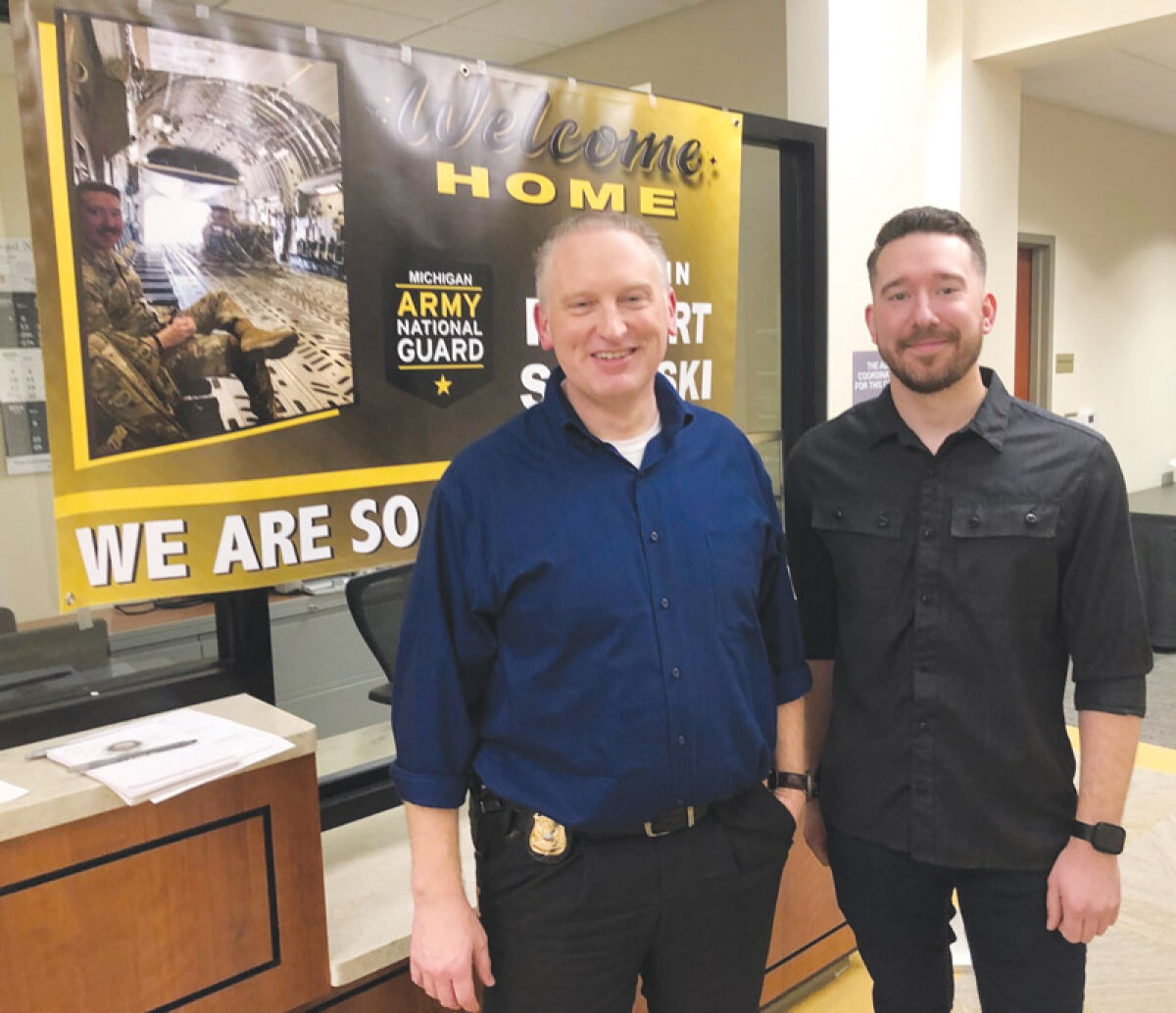  From left, Grosse Pointe City Public Safety Director John Alcorn stands with officer Robert Saleski in front of a poster welcoming him back from his deployment with the National Guard. 