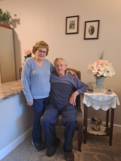  Janice and Dick Randall pose for a picture in their Novi apartment on Nov. 15, 2023. On the wall behind them are photos from their first engagement in 1951 and their wedding day on Oct. 25, 2006.  