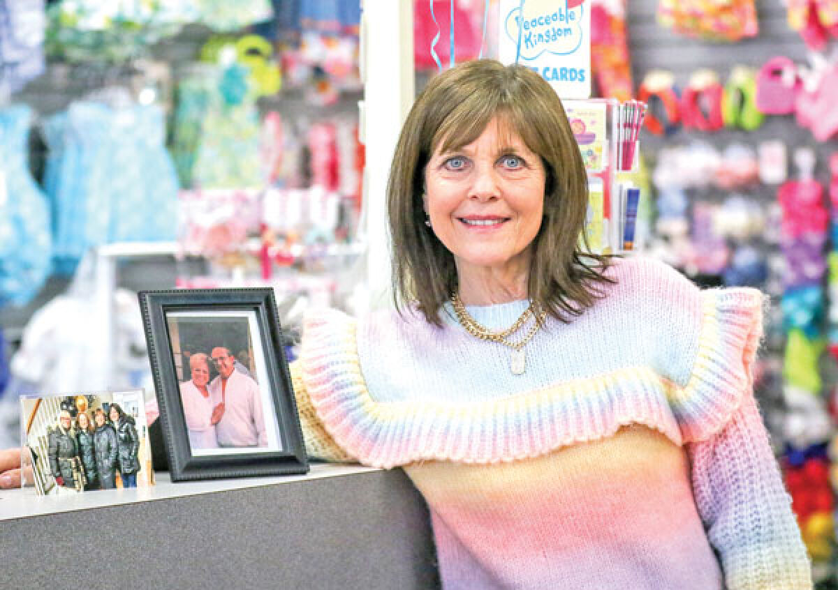 Denise Kort, owner of Connie’s Children’s Shop, poses with photos of her family. On the right are her parents, the previous owners of the shop, and on the left are Kort and her sisters, including Connie, the namesake of the shop, on the far left. 