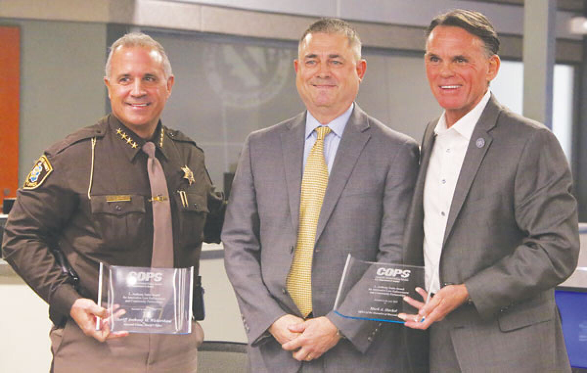  Macomb County Sheriff Anthony Wickersham, left, and county executive Mark Hackel, right, accept the 2023 L. Anthony Sutin Award at the Macomb County COMTEC center on March 12. The award was presented by Robert Chapman, deputy director of the Department of Justice’s Office of Community Oriented Policing Services. 