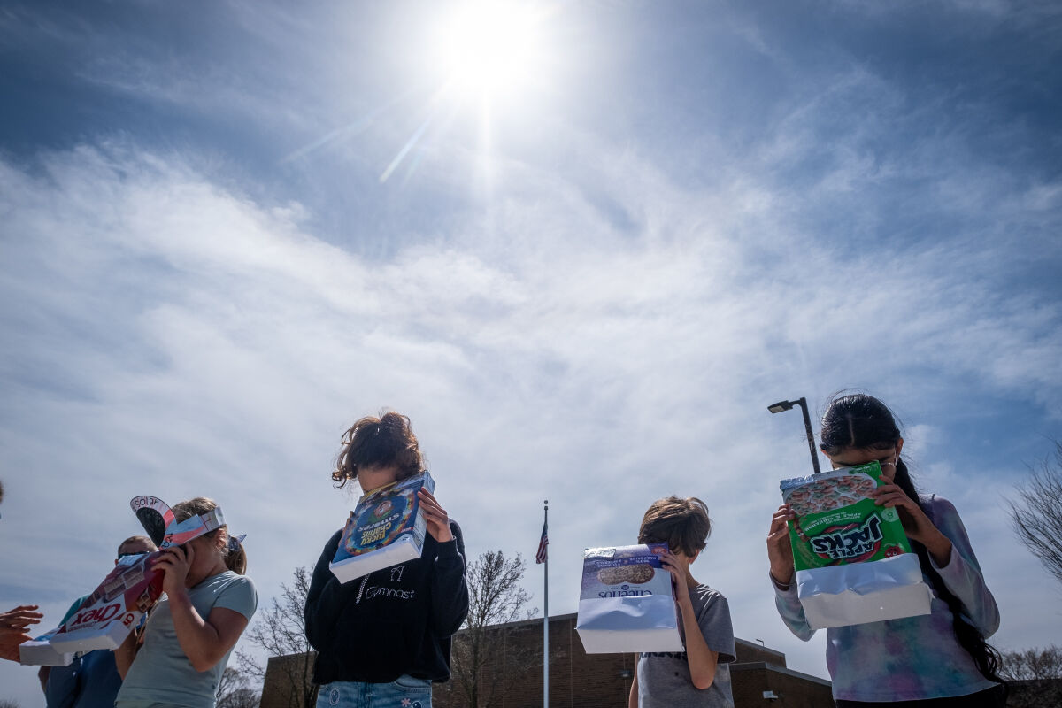  A group of fourth graders use pinhole viewers to watch the solar eclipse Monday, April 8, 2024, at Village Oaks Elementary School in Novi. 