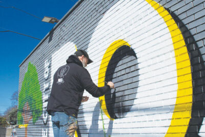  Mural artist Matthew Abraham touches up a mural on the side of Wing Snob April 7. The wall on Gratiot points toward Interstate 94 and welcomes drivers to Roseville. 