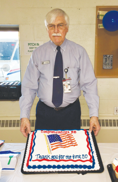  Ed Kane holds up a cake during a celebration of his  50 years at the post office. 