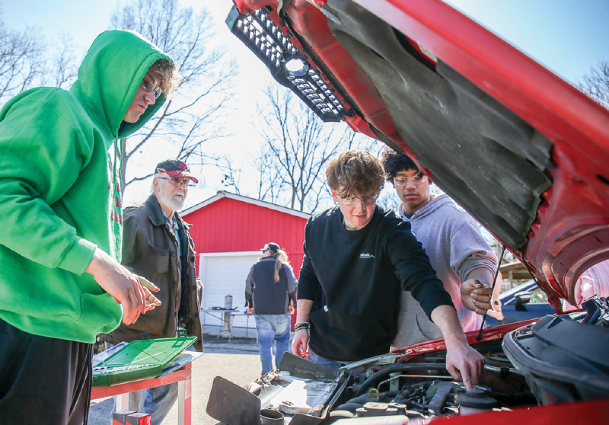  North Farmington High School auto shop students Cooper Matul, Joshua Tchozewski and Drake Laura remove a valve cover to replace the valve gasket for a client at the Redford Brightmoor Initiative in Detroit. 