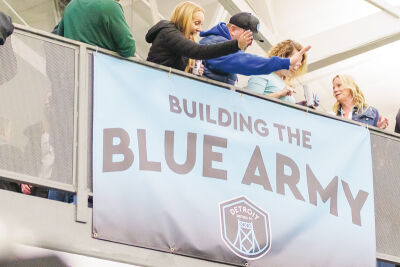  Spectators cheer behind a Detroit Metro Football Club sign at the team’s first game. 