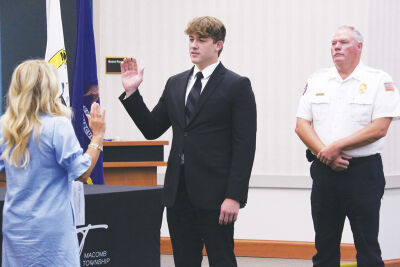  Macomb Township Clerk Kristi Pozzi, left, swears in Tyler Miller as a part-time firefighter on the morning of Aug. 14. Macomb Township Fire Department Chief Robert Phillips looks on. 