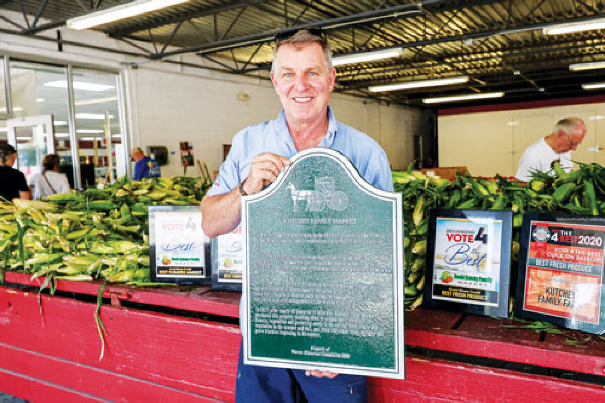  Standing in front of his produce and previous awards, David Kutchey holds the historical marker for Kutchey Family Market.  