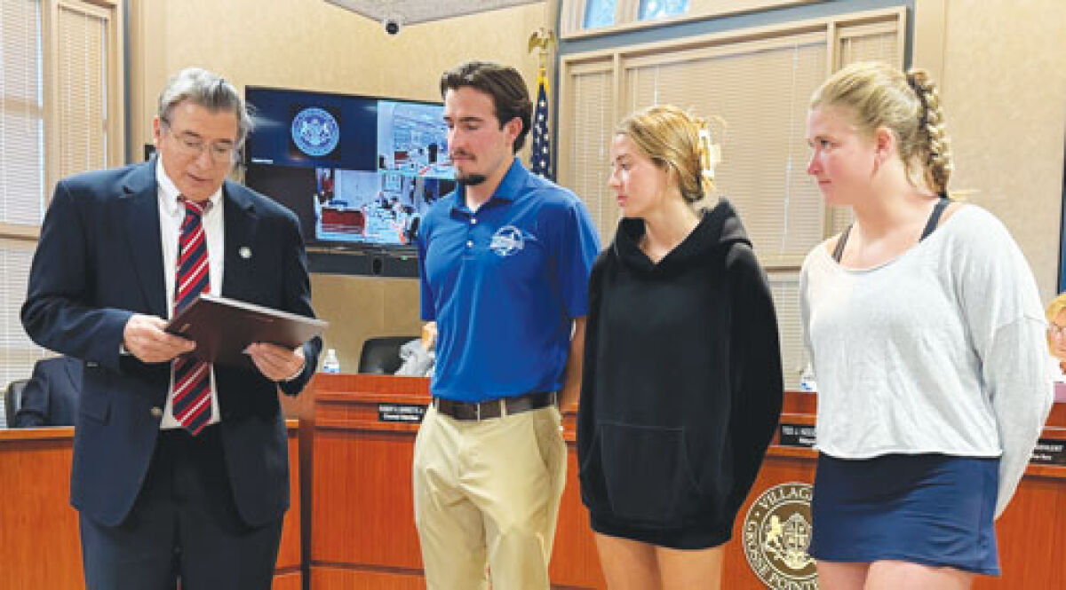  From left, Grosse Pointe Shores Mayor Ted Kedzierski reads a proclamation for the champion Sharks swim team as Coach Ben Van Vechten and team members Kennedy Hasting and Cailey Hard — both of whom are seniors who’ll graduate in 2026 — listen. 