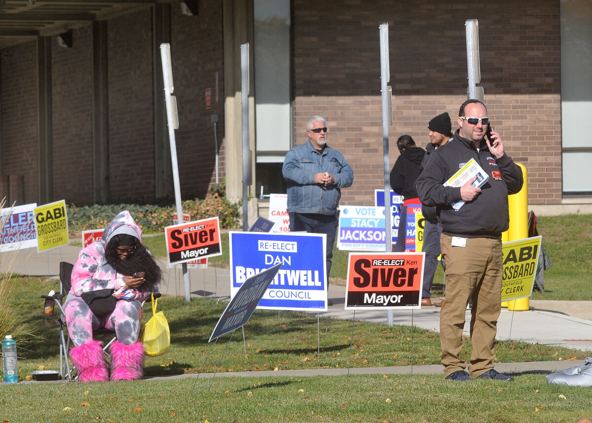  Politicians and campaign workers wait to greet voters outside Southfield City Hall on Election Day. 