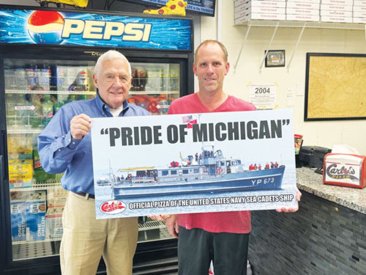  Capt. Luke Clyburn and Carlo’s Pizza owner Matt Warnke hold up a sign for the Pride of Michigan inside of the pizza shop.  