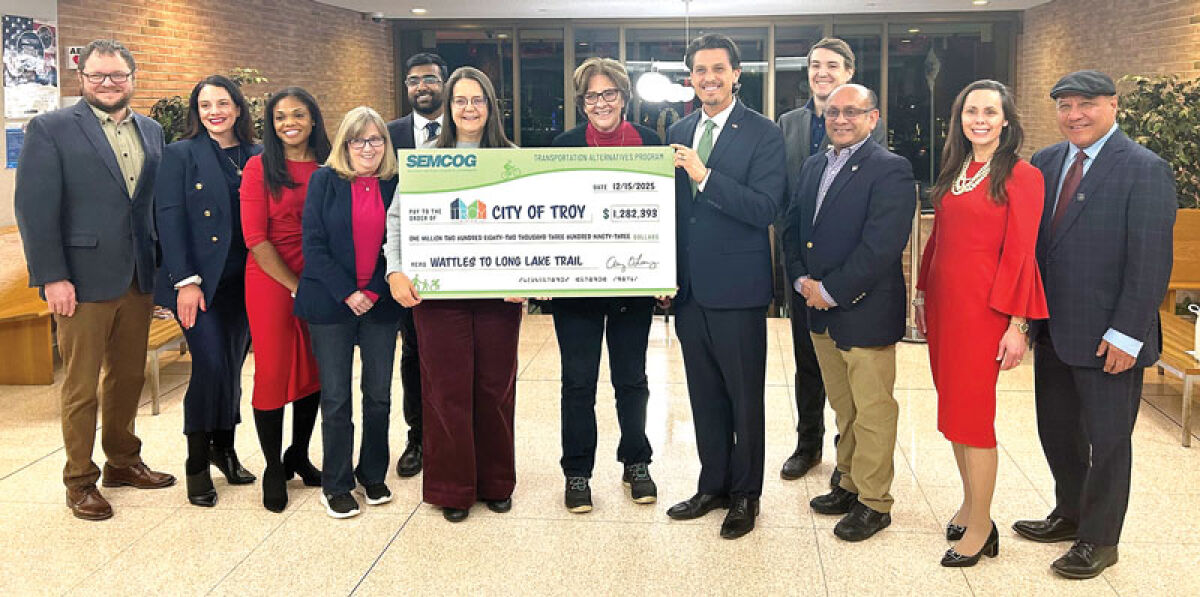  SEMCOG Executive Director Amy O’Leary, left, gathers around the check with Oakland County Commissioner Gwen Markham and Troy Mayor Ethan Baker. 